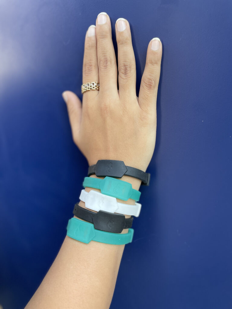 Hand wearing five Tapr bands in multiple colours, against a plain wall.